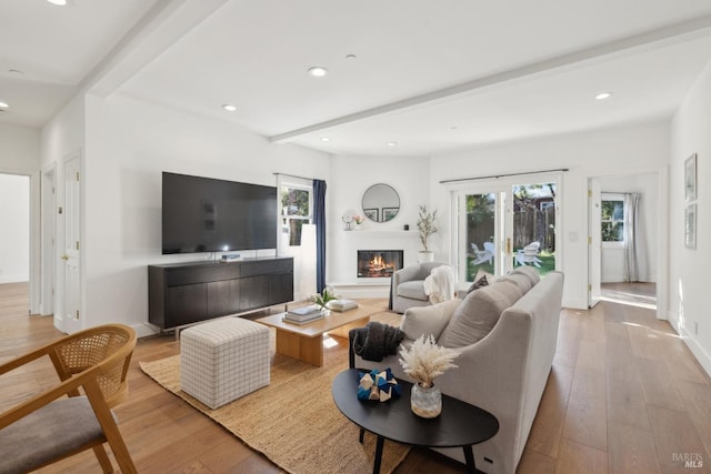 living area featuring beamed ceiling, a glass covered fireplace, hardwood / wood-style flooring, and recessed lighting