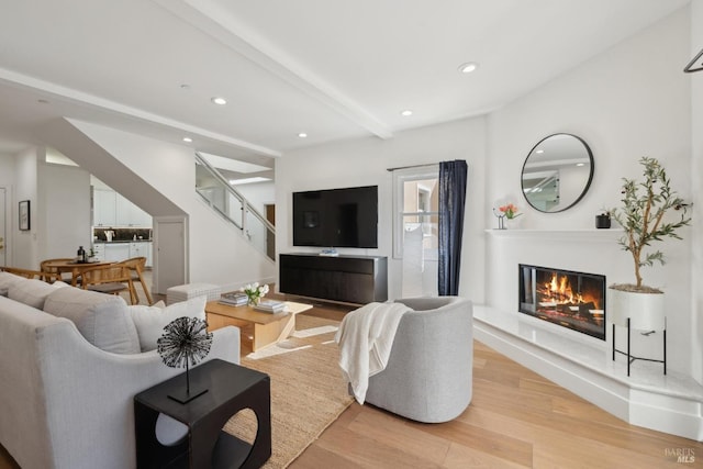 living area featuring recessed lighting, a glass covered fireplace, light wood-type flooring, beamed ceiling, and stairs