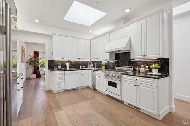 kitchen with a skylight, dishwasher, dark countertops, ventilation hood, and gas stove