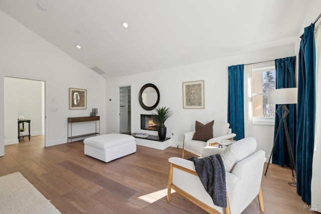 living area with a glass covered fireplace, wood finished floors, visible vents, and recessed lighting