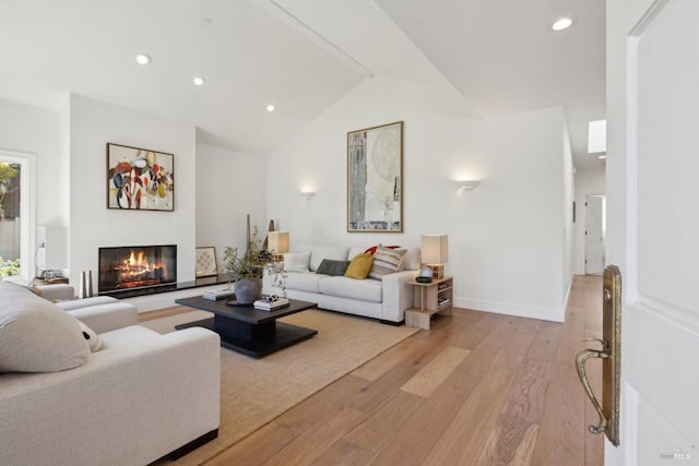 living room with lofted ceiling, light wood-style flooring, recessed lighting, baseboards, and a glass covered fireplace