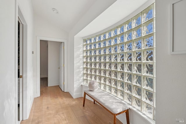 corridor featuring baseboards, vaulted ceiling, and light wood finished floors