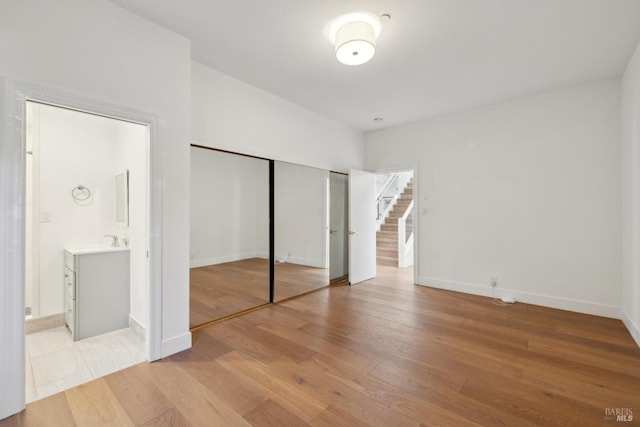 unfurnished bedroom featuring a closet, a sink, light wood-style flooring, and baseboards