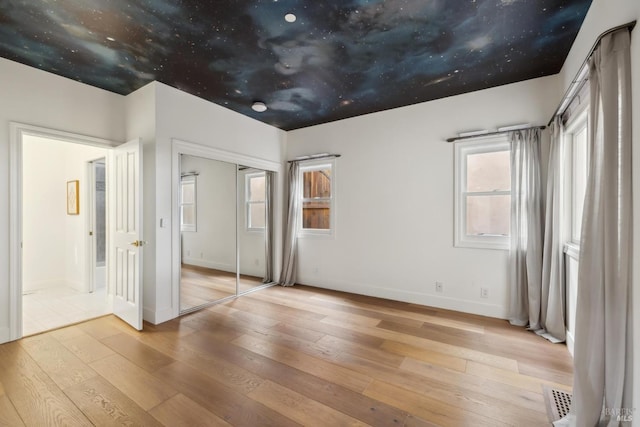 unfurnished bedroom with hardwood / wood-style floors, a closet, visible vents, and baseboards