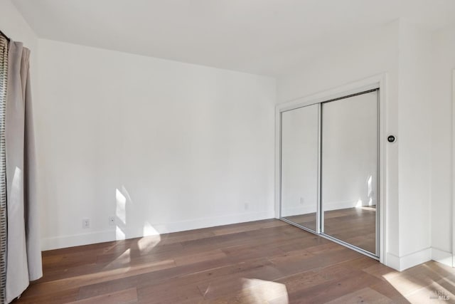 unfurnished bedroom with a closet, wood finished floors, and baseboards