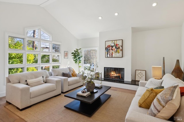 living area with high vaulted ceiling, a glass covered fireplace, wood finished floors, and recessed lighting