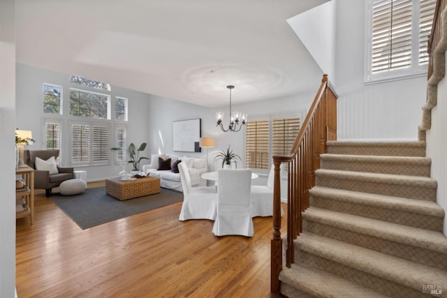 living area featuring stairway, plenty of natural light, an inviting chandelier, and wood finished floors