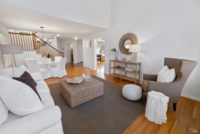 living area featuring baseboards, stairway, an inviting chandelier, and wood finished floors