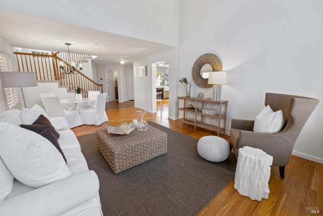 living room with baseboards, wood finished floors, an inviting chandelier, and stairway