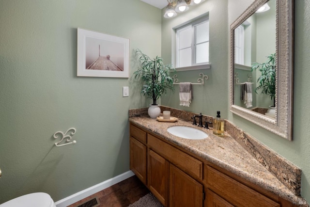 bathroom with baseboards, toilet, vanity, and visible vents