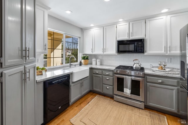 kitchen with tasteful backsplash, gray cabinetry, a sink, light stone countertops, and black appliances