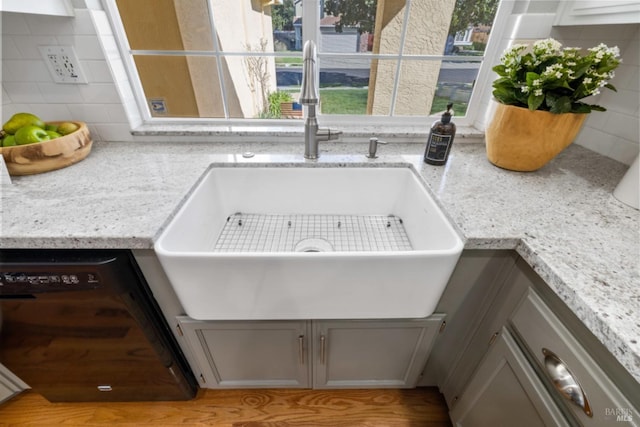 interior details with gray cabinetry, a sink, black dishwasher, light stone countertops, and tasteful backsplash