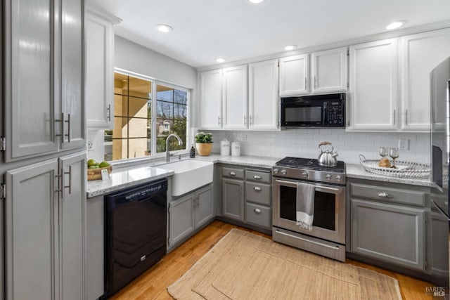 kitchen with light stone counters, a sink, gray cabinetry, and black appliances