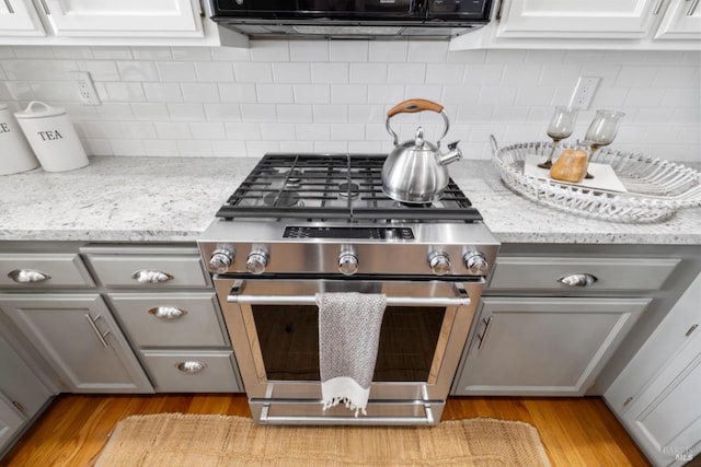 kitchen with stainless steel gas range, light wood finished floors, backsplash, and gray cabinetry