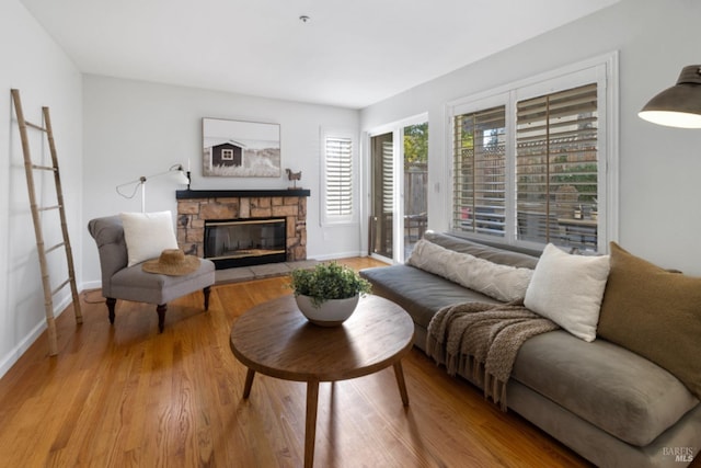 living room featuring baseboards, a stone fireplace, and light wood-style floors