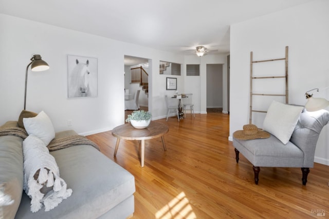 living room with a ceiling fan, baseboards, light wood finished floors, and stairs