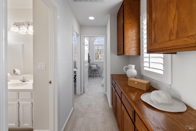 corridor featuring light carpet, a sink, visible vents, baseboards, and recessed lighting