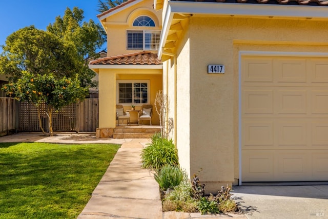 property entrance featuring a garage, a tiled roof, fence, a yard, and stucco siding