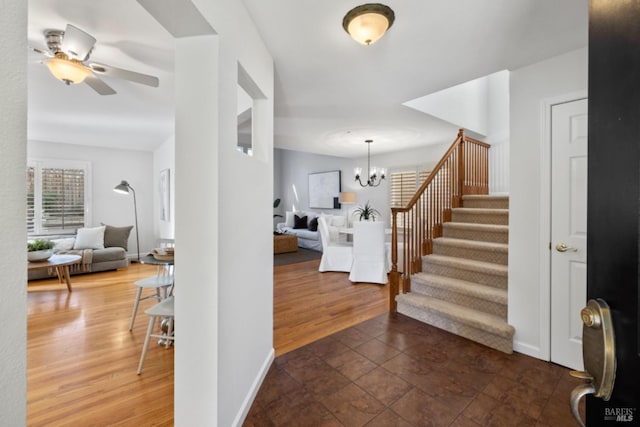 entryway with ceiling fan with notable chandelier, wood finished floors, baseboards, and stairs