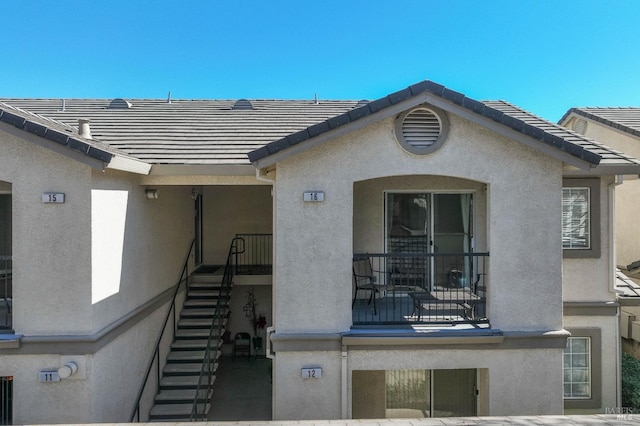 back of house featuring stairs, a tiled roof, and stucco siding