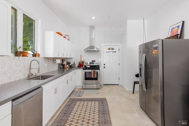 kitchen featuring tasteful backsplash, wall chimney exhaust hood, appliances with stainless steel finishes, white cabinetry, and a sink