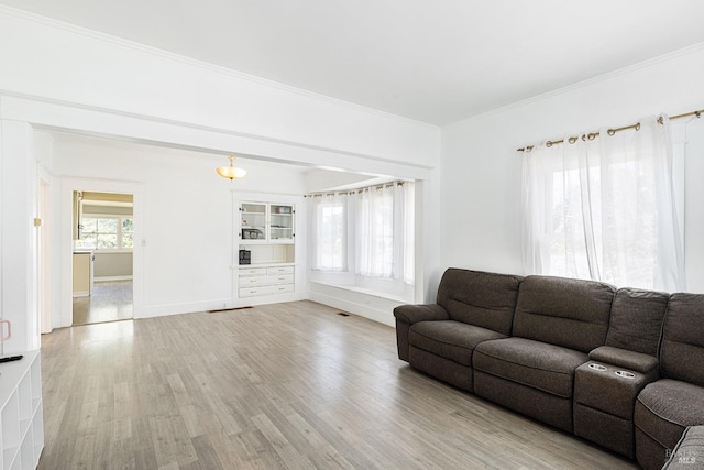 unfurnished living room featuring built in features, crown molding, light wood-style flooring, and baseboards