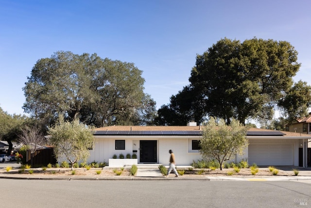 ranch-style home with an attached garage, driveway, and roof mounted solar panels