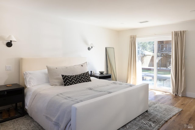 bedroom with wood finished floors, visible vents, and access to exterior