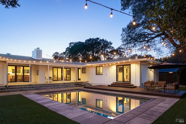 back of house at dusk with entry steps, a wooden deck, an outdoor pool, a chimney, and a patio area