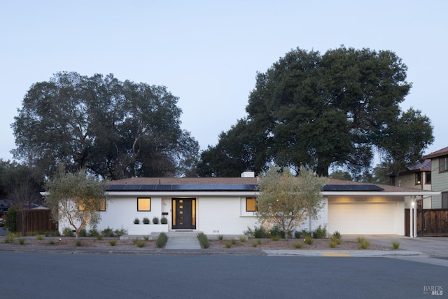 view of front of property featuring a garage, driveway, fence, and solar panels