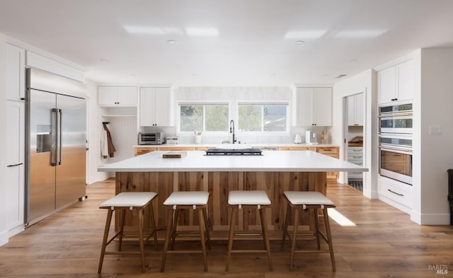 kitchen featuring stainless steel appliances, white cabinets, light wood-style floors, and a kitchen island