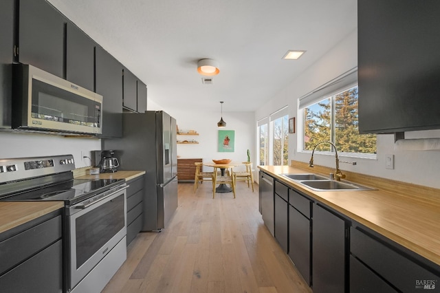 kitchen featuring light wood-style flooring, stainless steel appliances, a sink, light countertops, and dark cabinetry