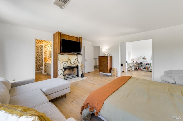 bedroom with light wood-type flooring, visible vents, a fireplace, and ensuite bath