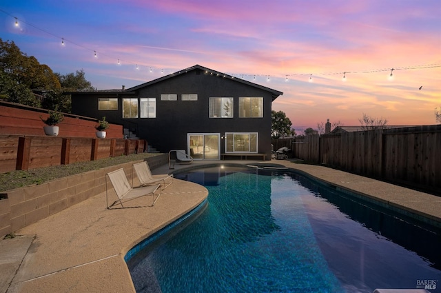 pool at dusk featuring a pool with connected hot tub, a fenced backyard, and a patio