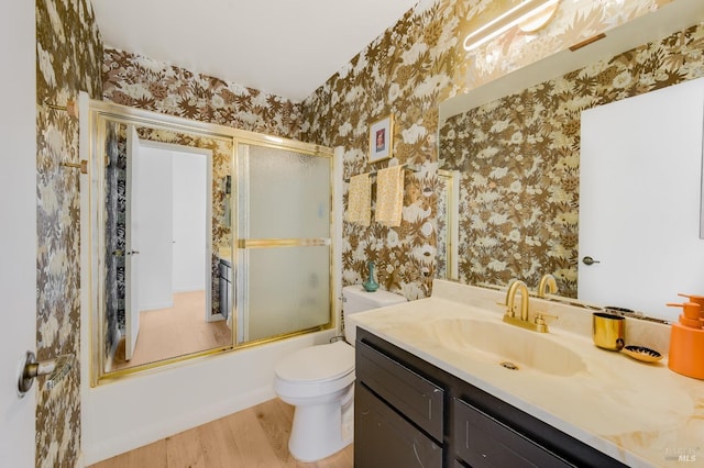 full bathroom featuring bath / shower combo with glass door, toilet, vanity, wood finished floors, and wallpapered walls