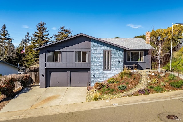 view of front of home with a garage, concrete driveway, a chimney, roof with shingles, and fence