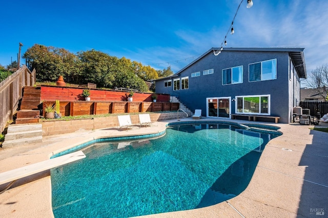 view of swimming pool featuring a patio, a fenced backyard, stairway, a pool with connected hot tub, and a diving board