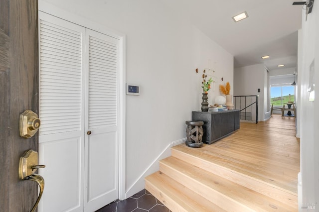 hall with wood finished floors, an upstairs landing, and baseboards