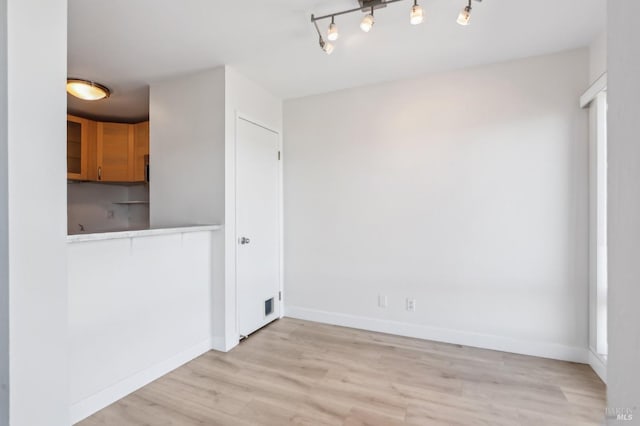 unfurnished room featuring track lighting, light wood-type flooring, and baseboards