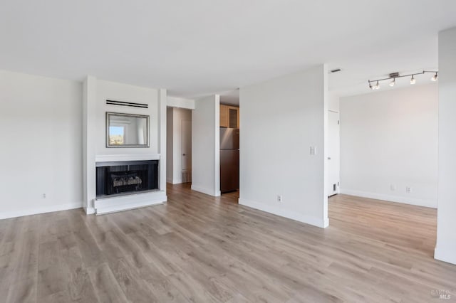 unfurnished living room featuring baseboards, a fireplace with raised hearth, and light wood finished floors