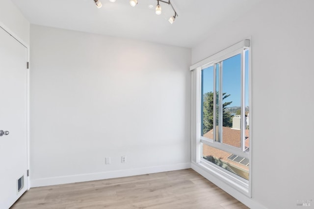 unfurnished room with track lighting, visible vents, light wood-style flooring, and baseboards