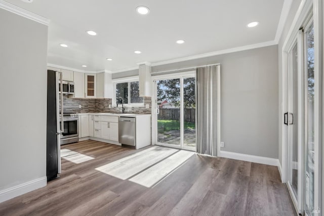 kitchen with wood finished floors, baseboards, ornamental molding, appliances with stainless steel finishes, and tasteful backsplash