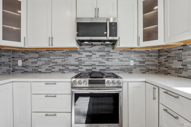 kitchen featuring tasteful backsplash, white cabinetry, appliances with stainless steel finishes, light countertops, and glass insert cabinets