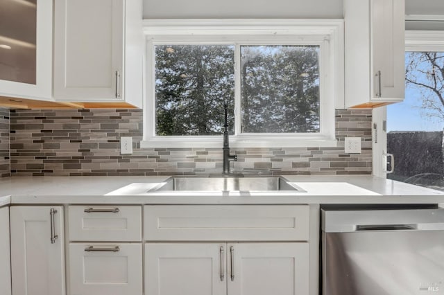 kitchen with plenty of natural light, stainless steel dishwasher, white cabinetry, light countertops, and decorative backsplash