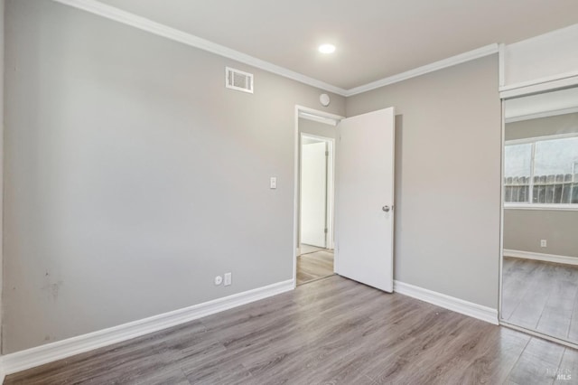 unfurnished bedroom with crown molding, wood finished floors, visible vents, and baseboards