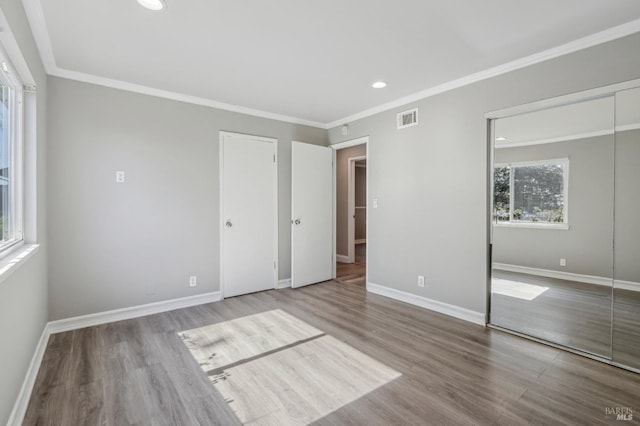 unfurnished bedroom with visible vents, ornamental molding, baseboards, and wood finished floors