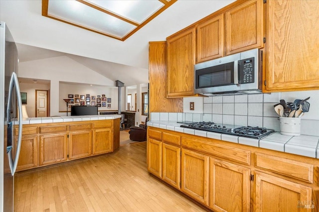 kitchen featuring lofted ceiling, light wood-type flooring, tile countertops, and appliances with stainless steel finishes