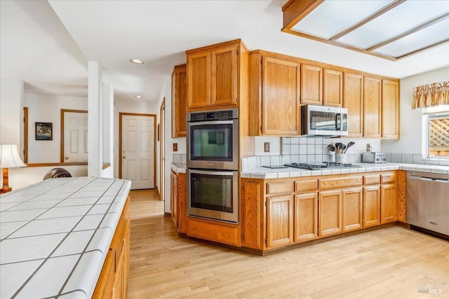 kitchen with recessed lighting, appliances with stainless steel finishes, light wood-type flooring, backsplash, and tile counters