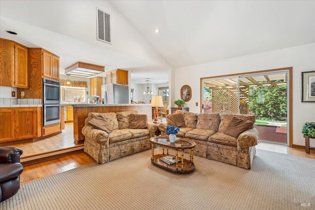 living area with high vaulted ceiling, light wood-type flooring, and visible vents