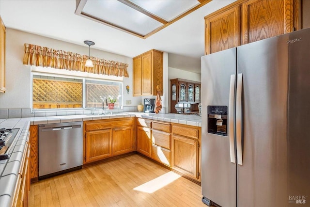 kitchen with brown cabinets, decorative light fixtures, stainless steel appliances, light wood-type flooring, and a sink